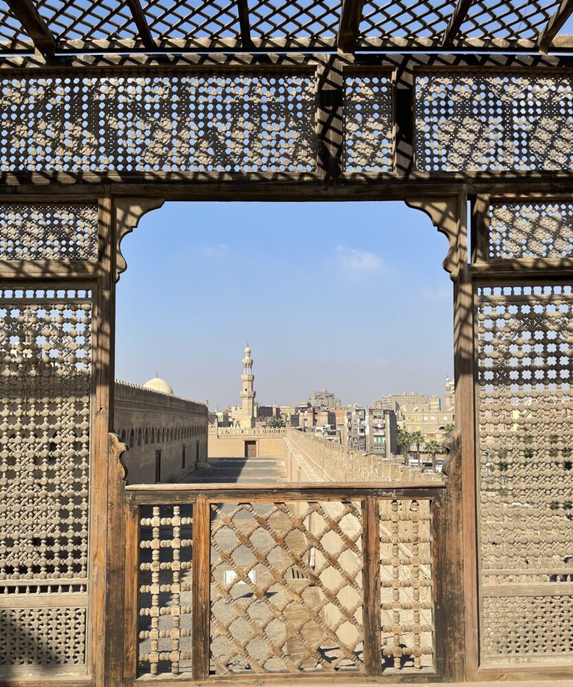Mosque minaret against a blue sky framed by patterned wooden lattice screens.
